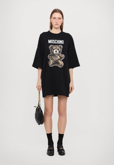 Svart oversized t-shirt klänning med en björngrafik och "MOSCHINO" text. Korta ärmar, mjukt bomullsmaterial och lös passform.