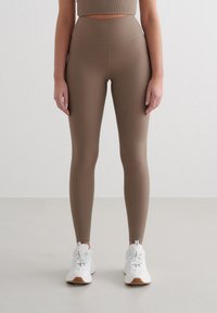 Leggings rayés marron avec une taille haute, présentant une texture lisse. Associés à des chaussures de sport blanches pour un look coordonné.