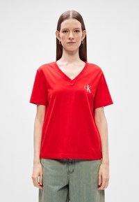 Červené bavlnené tričko s dizajnom v-výstrihu a krátkymi rukávmi. Na ľavej strane hrude sa nachádza malé biele logo CK. Uvoľnený strih.