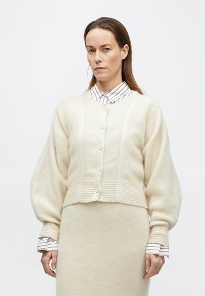 Kreemikas villane kardigan, pehmest villast, millel on nööbitav esiosa, soonikuline tekstuur ja pallikujulised varrukad. Kandmiseks kihina triibulise särgi peal.