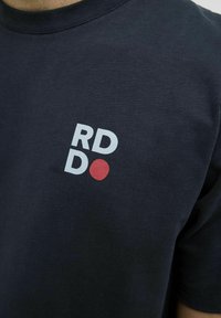 Navyblå bomulds T-shirt med et lille hvidt og rødt grafisk logo på forsiden, rund halsudskæring og korte ærmer.