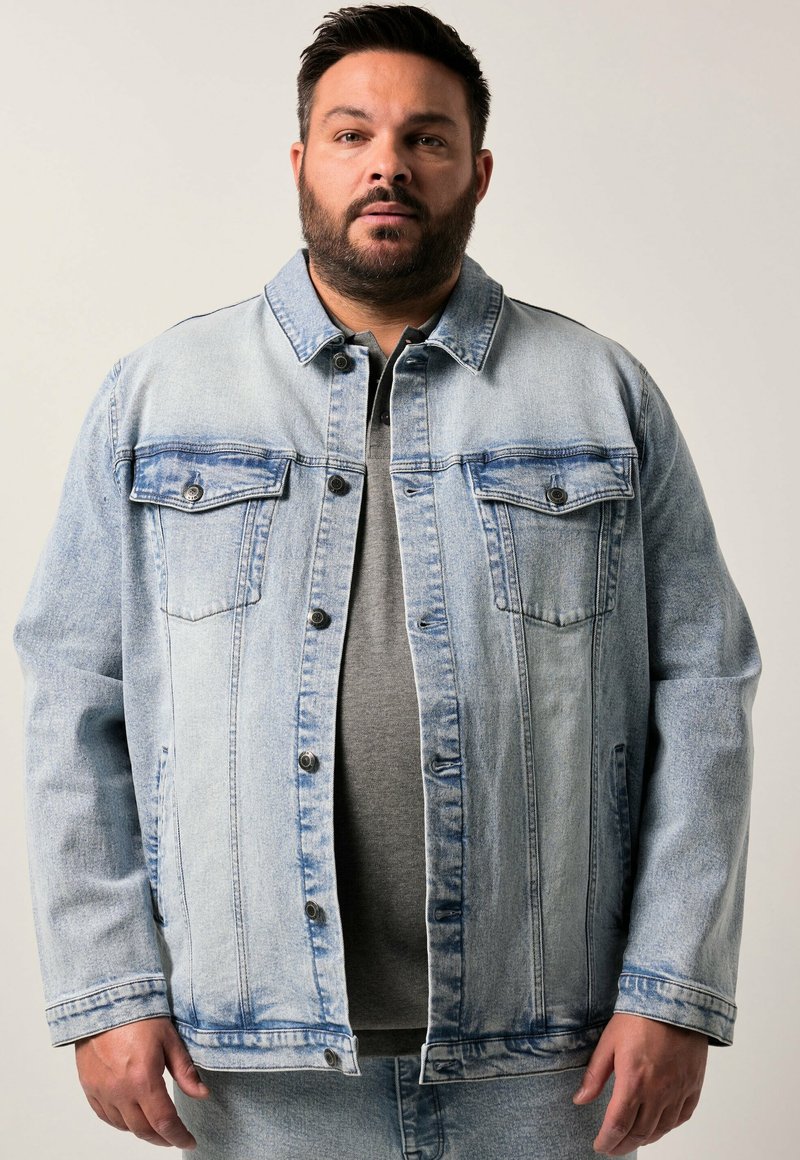 Chaqueta de mezclilla azul clara con cierre de botones, dos bolsillos en el pecho y un corte relajado, que presenta acentos desgastados y un diseño de cuello clásico.