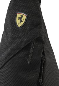 Sac en tissu noir avec un motif en losanges texturé. Comprend un bouclier logo Ferrari jaune et noir bien visible ainsi qu'un cordon de serrage ajustable.