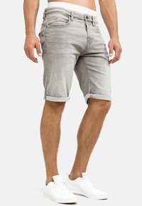 Lichtgrijze denim shorts met opgerolde zoom, voorzien van zijzakken en subtiele slijtplekken. Gekleed met witte sneakers.