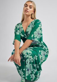 Vihreä kukallinen kietaisumekko lyhyillä hihoilla, jossa on suuria vaaleansinisiä kukkia ja V-mallinen kaula-aukko. Valmistettu kevyestä kankaasta, sileä rakenne.