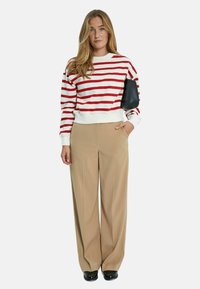 Felpa cropped a righe rosse e bianche con polsini a coste, abbinata a pantaloni a gamba larga beige a vita alta e borsa nera.