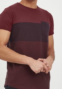 Bordeaux-gestreifter T-Shirt mit kurzen Ärmeln, rundem Halsausschnitt und kleiner Brusttasche. Aus weichem Baumwollstoff mit strukturierter Oberfläche gefertigt.