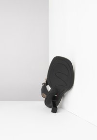 Black high-heeled sandal with a chunky heel and ankle strap. The sole has a textured design and features logo detailing in color.