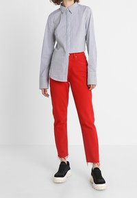 Camisa de botones a rayas en azul y blanco, combinada con unos vaqueros rojos cortos y zapatillas negras con suelas blancas. Dobladillo deshilachado en los vaqueros.
