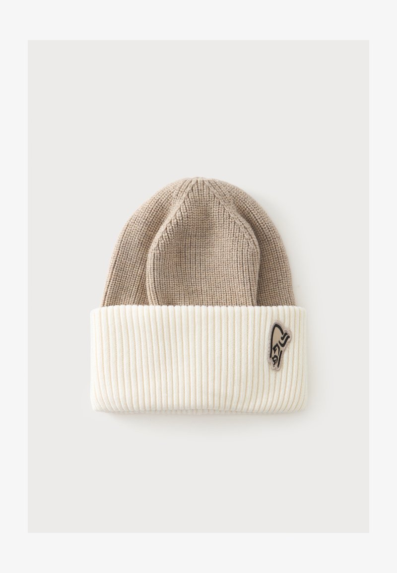 Bonnet beige en maille avec large bord-côte blanc replié et petite écusson logo noir et beige sur le bord, sur fond clair.
