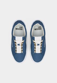 Ζευγάρι μπλε τζιν αθλητικά παπούτσια με λευκά κορδόνια και σόλες, χρυσά κορδόνια, και το "LOVE MOSCHINO" τυπωμένο στο εσωτερικό και στα πλαϊνά.