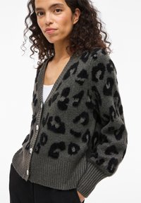 Καζάκι σε σκούρο πράσινο, με χνουδωτό λιονταρίσιο σχέδιο σε μαύρο. Ριμπ λάστιχο στους αγκώνες και το στρίφωμα; κούμπωμα με κουμπιά; μαλακή υφή.