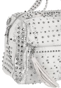 Bolso de cuero blanco con textura adornado con tachuelas y picos de plata, con cierre de cremallera y un fleco decorativo.