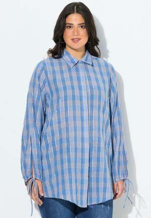 Blusa de cuadros azul claro con mangas largas, cuello y lazos ajustables en los puños. Confeccionada en una tela texturizada y tejida.