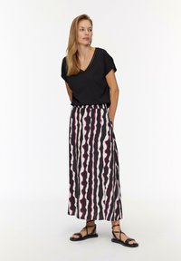 Zwarte v-hals t-shirt gecombineerd met een lange rok met afwisselend zwarte, witte en roze golvende strepen. Zwarte platte sandalen maken de look af.