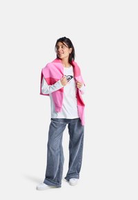 Modelka ma na sobie różowy sweter w kolorowe bloki, zarzucony na białą koszulę z długim rękawem, połączony z dżinsami z szerokimi nogawkami i białymi sneakersami.