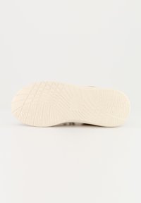 Helle beige Sneakersohle mit strukturierten Griffmustern, runder Form und glatter Oberfläche sowie dezenten Markenakzenten.