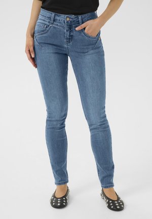 Slim-fit sinised teksad, millel on keskmise tõusuga vöökoht, ees taskud ja peen kulumine. Kantud mustade tasaste kingadega, millel on hõbedased nurgad.