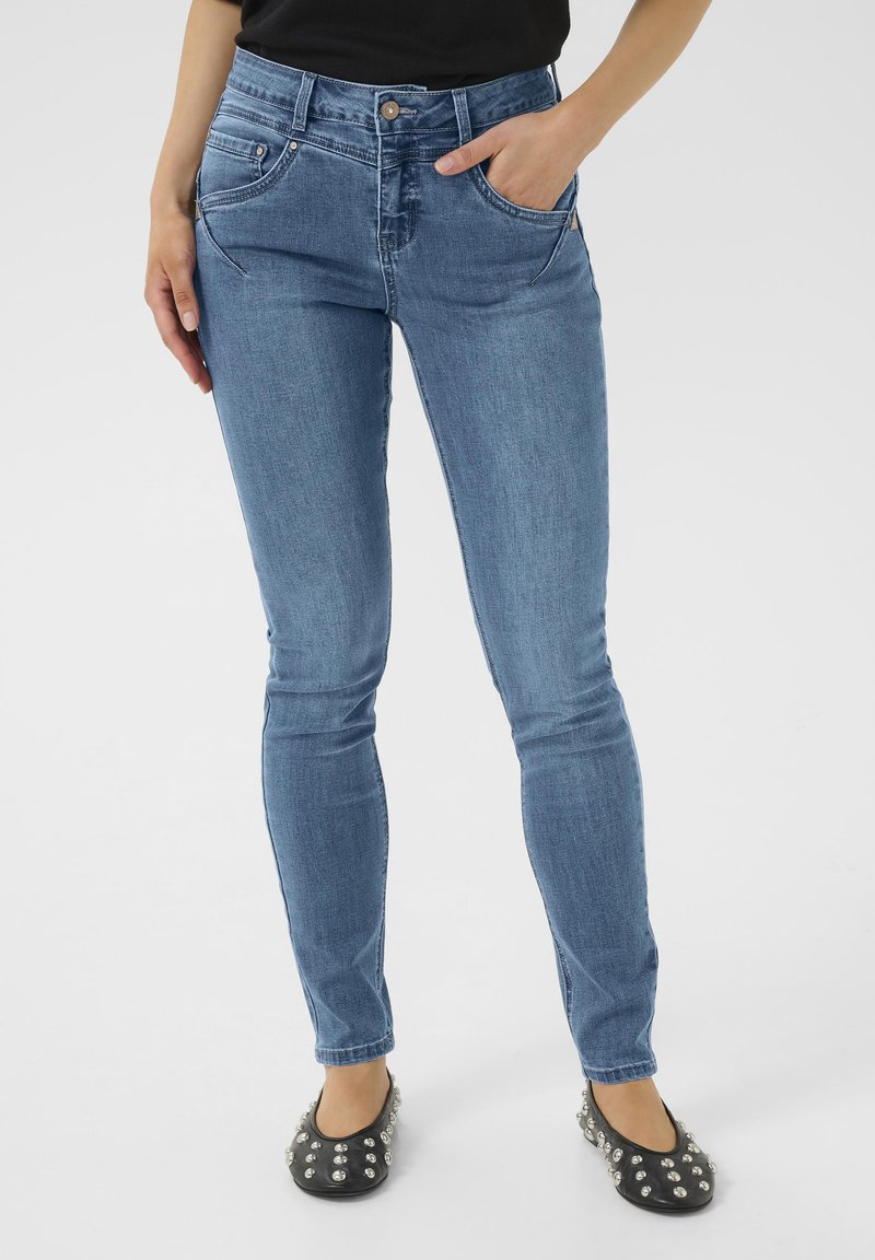 Slim-fit modré džíny s střední výškou pasu, předními kapsami a jemným vyblednutím. Kombinováno s černými balerínami se stříbrnými hroty.