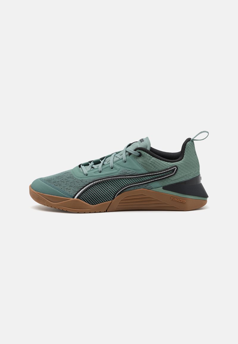 Zapatilla deportiva verde y negra con parte superior de malla, suela de goma, patrones texturizados y collar acolchado; cuenta con cordones y una lengüeta en el talón.