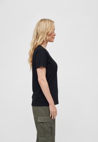 Svart T-skjorte med kort erm og rund hals, laget av mykt stoff, kombinert med olivengrønne cargo-bukser med sidelommer.