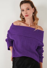 Pullover viola a spalle scoperte in maglia con trama a costine, maniche ampie e vestibilità rilassata, abbinato a una collana con perle.