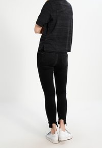 Svart kortärmad t-shirt med korta ärmar och texturerad yta, kombinerad med åtsittande svarta jeans med fransiga sömmar och vita sneakers.