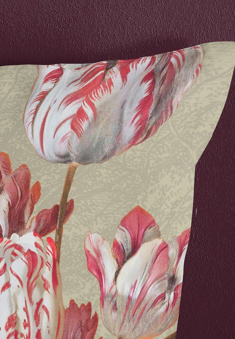 Nära bild av tyg med stora tulpanblommor i röda, vita och rosa nyanser mot en beige mönstrad bakgrund och en mörkröd yta.