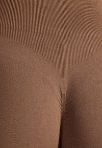 Leggings marroni a coste con fascia alta in vita, dalla texture liscia e un design aderente che mette in risalto le forme del corpo.