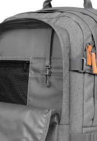 Zaino grigio con tessuto testurizzato, compartimento con zip, tasca in rete e tracolla regolabile con dettagli in pelle.