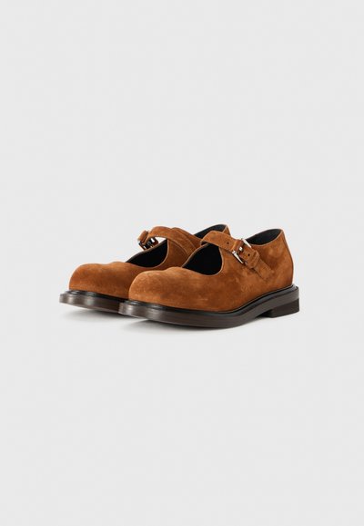Brown suede Mary Jane shoes with a rounded toe, adjustable buckle strap, and a dark, chunky sole. Smooth texture with minimal detailing.