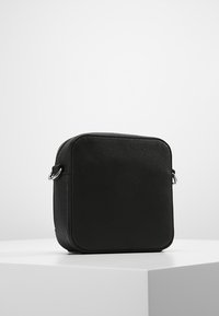 Borsa a tracolla nera in materiale sintetico testurizzato, dotata di zip e accessori in metallo. Design semplice e minimalista.