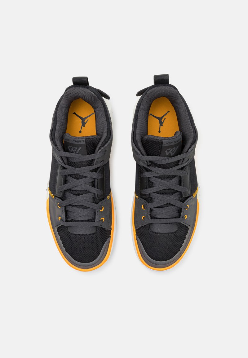 Zapatillas negras y grises con acentos naranjas. Presentan materiales de malla y sintéticos, puntera redonda, cordones planos y logotipo visible en la lengua.