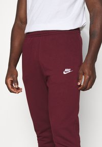 Vinröda Nike sweatpants med resår i midjan, sidofickor och vit logga. Gjorda av mjukt tyg, med avsmalnande passform.