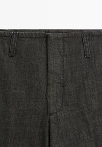 Pantalon en denim noir avec un design classique à cinq poches, une coupe droite, et une texture subtile agrémentée de coutures contrastantes.