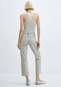 O persoană cu păr scurt blond poartă un tricou gri fără mâneci, blugi scurți gri deschis cu margini brut, și balerini metalici argintii, stând cu spatele.