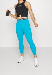 Top cropped nero con logo, abbinato a leggings blu brillante con un elastico brandizzato. Scarpe da ginnastica bianche con dettagli neri.