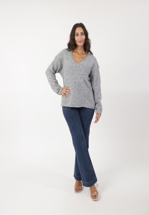 Suéter gris de punto con un escote en V, combinado con jeans de mezclilla oscuros de corte acampanado y sandalias de tacón alto transparentes. Conjunto simple y casual.