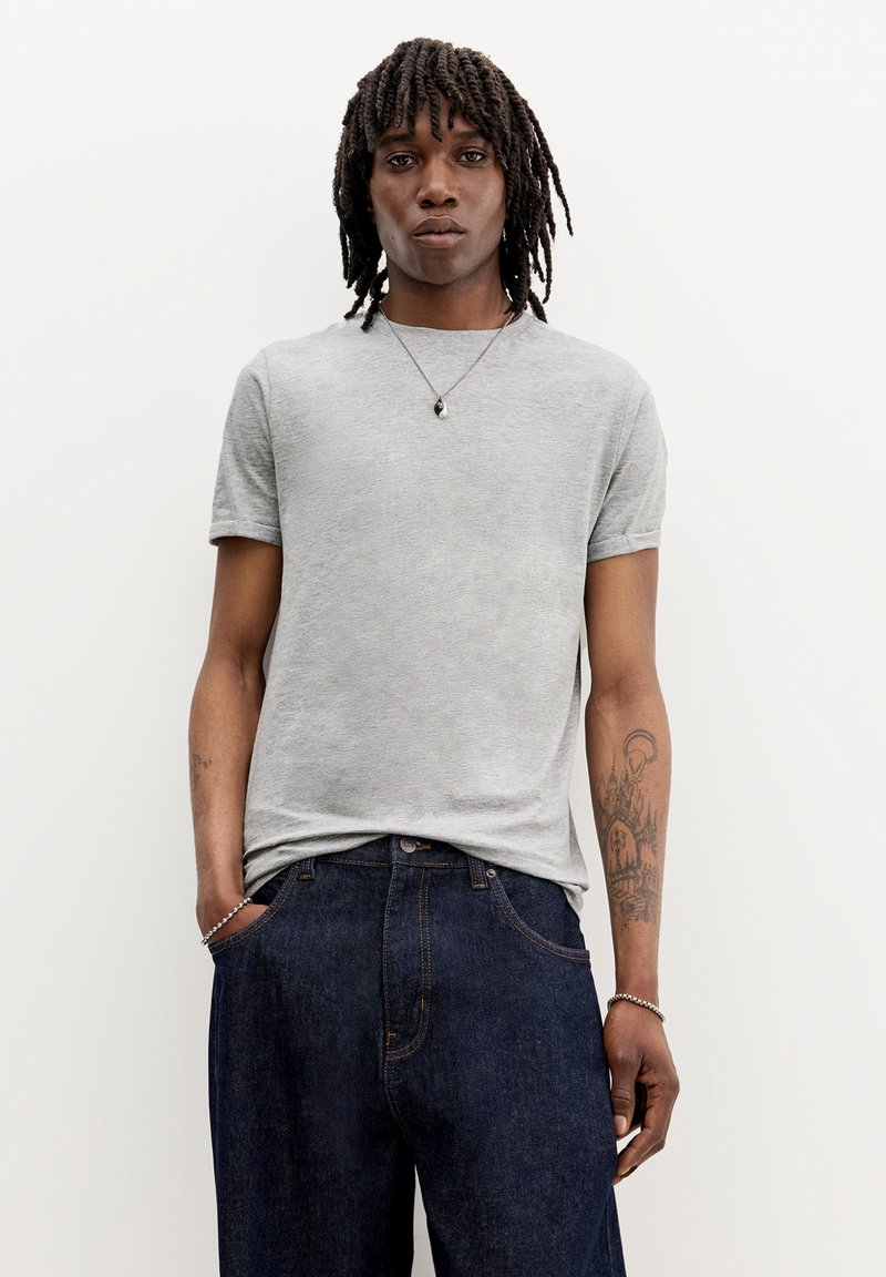 Cămașă gri cu mâneci scurte, cu guler rotund, asociată cu blugi din denim de culoare bleumarin. Prezintă o textură subtilă și un design minimalist.