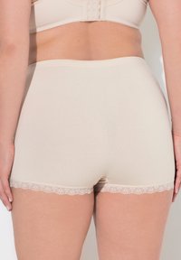 Pantaloni corti in cotone beige con vita alta e delicata rifinitura in pizzo all'orlo. Texture liscia, design aderente e stile minimalista.