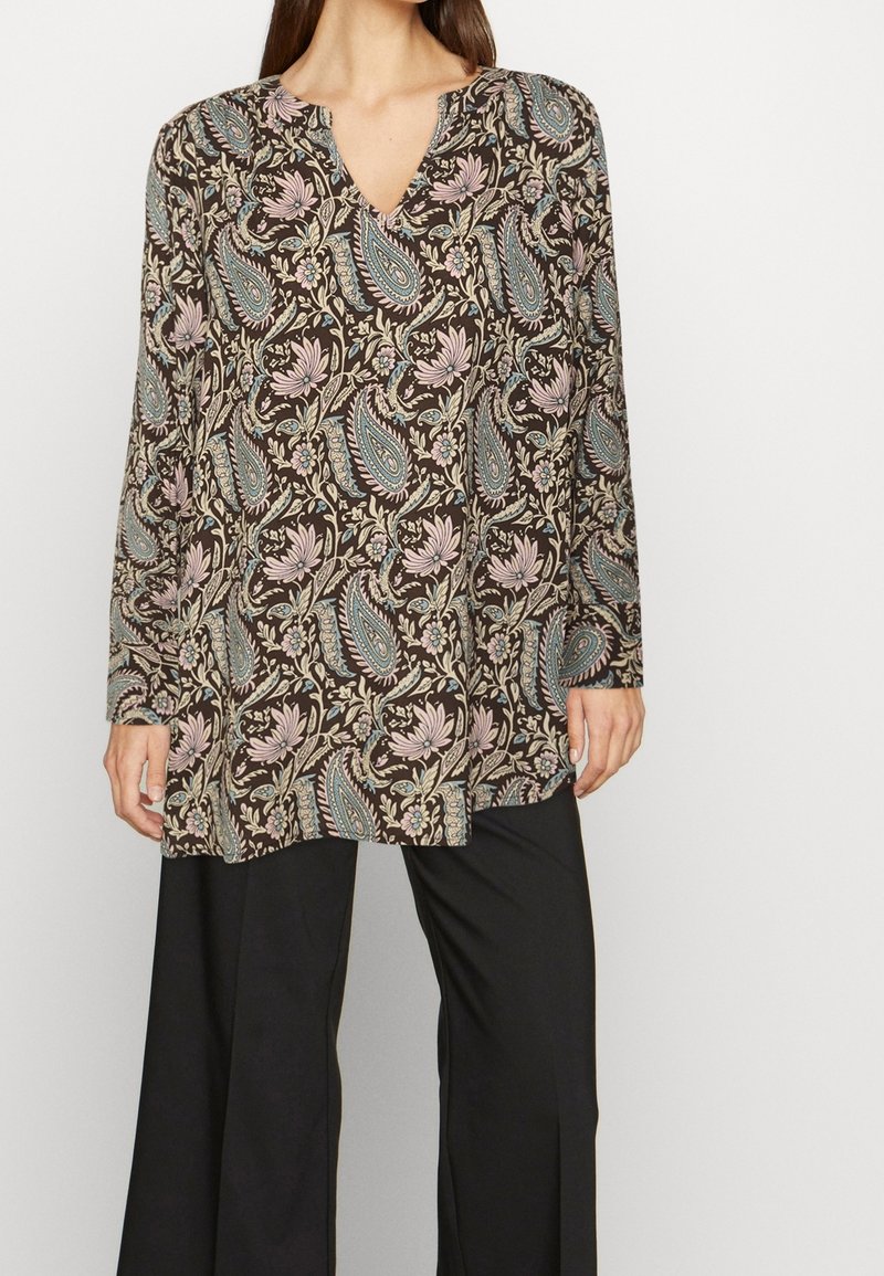 Túnica de mangas largas en tela marrón con un patrón floral de paisley en azul claro y rosa. Cuello en V y corte relajado. Combinada con pantalones negros.
