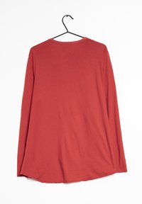 Chemise rouge à manches longues en tissu doux, avec un col rond et un ourlet arrondi, présentée sur un cintre noir sur un fond blanc.