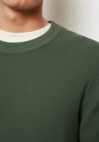 Zielony sweter w żeberkowy wzór z teksturowanym wykończeniem i kontrastowym białym dekoltem w kształcie łódki. Pokazuje zbliżenie na detale tkaniny i dekoltu.