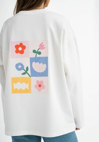 Weißes Sweatshirt mit langen Ärmeln, das ein farbenfrohes grafisches Design mit Blumen und Formen in Pink, Rot, Blau und Gelb auf dem Rücken zeigt.