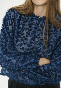Marineblauwe blouse van textuur met gerimpeld materiaal, lange mouwen en een knoopsluiting bij de nek. Transparant ontwerp met ingewikkelde patronen.