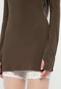 Smeđi dugi rukav majica od glatkog materijala, složena preko kratkih hlača od bijele čipke s cvjetnim uzorkom.