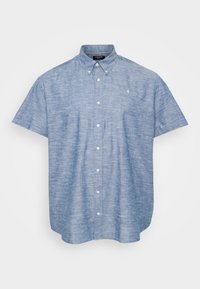 Camisa de botones de manga corta en tela chambray azul claro, con un cuello estructurado, botones frontales y un pequeño emblema en el pecho.