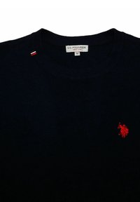 Pull en maille bleu marine avec un col rond côtelé. Présente un logo rouge brodé sur la poitrine et une petite étiquette rouge, blanche et bleue au cou.