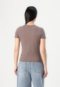 Brunet tettskjorte med korte ermer, rund hals, og glatt tekstur, kombinert med lys blå høyt liv jeans. Minimalistisk design.