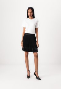 White short-sleeve top with button accents paired with a black pleated skirt and black high-heeled shoes. Smooth, lightweight materials.